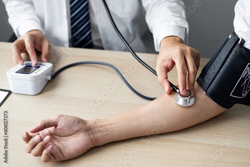 The doctor is sitting at workplace and using a pressure gauge to measuring the blood pressure of the patient.