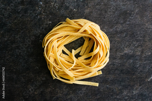 One Single Tagliatelle Pasta Nest on a Dark Background: A pasta nest of dried noodles viewed closeup from directly above