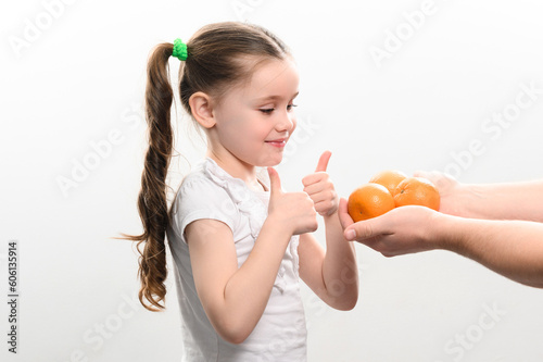 A little girl is given tangerines on a white background, the child takes tangerines.