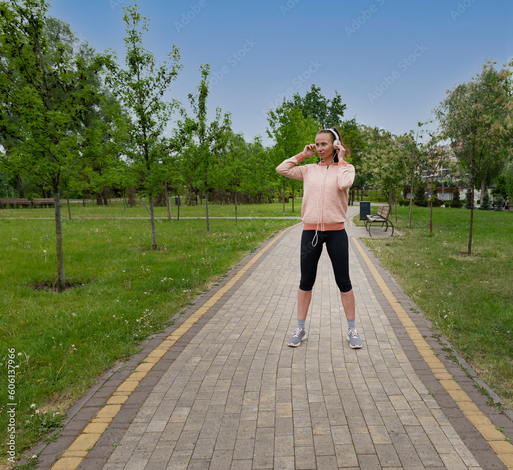 Young athletic woman stands on the road in the park. woman listening to music and exercising. Woman workout park