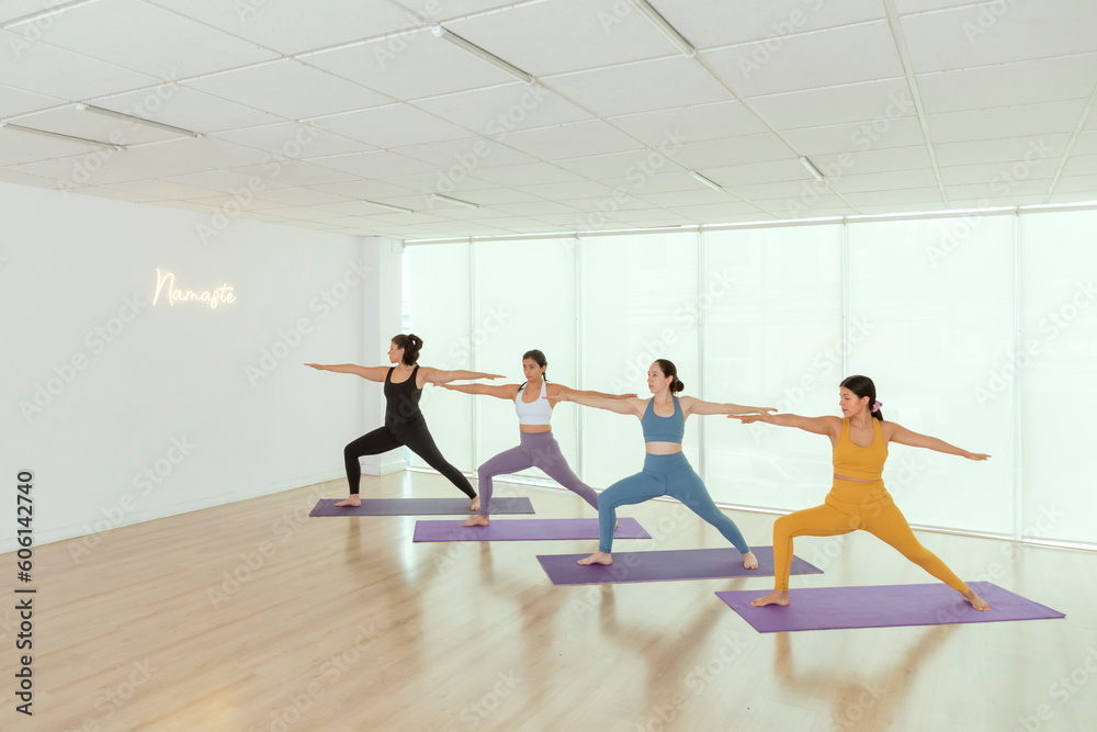 group of women doing the warrior pose while practicing yoga in a studio