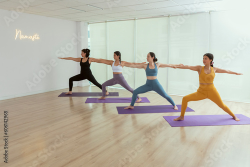 group of women doing the warrior pose while practicing yoga in a studio