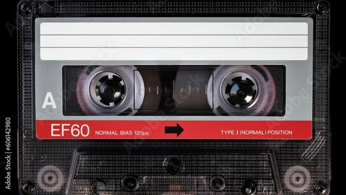 Audio cassette tape in use for sound recording in the tape recorder. A vintage, brand new blank red labelled music cassette playing back in a deck player. Static video camera shot. Close up, 4K

