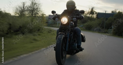 Male biker riding a retro motorcycle on a countryside road.