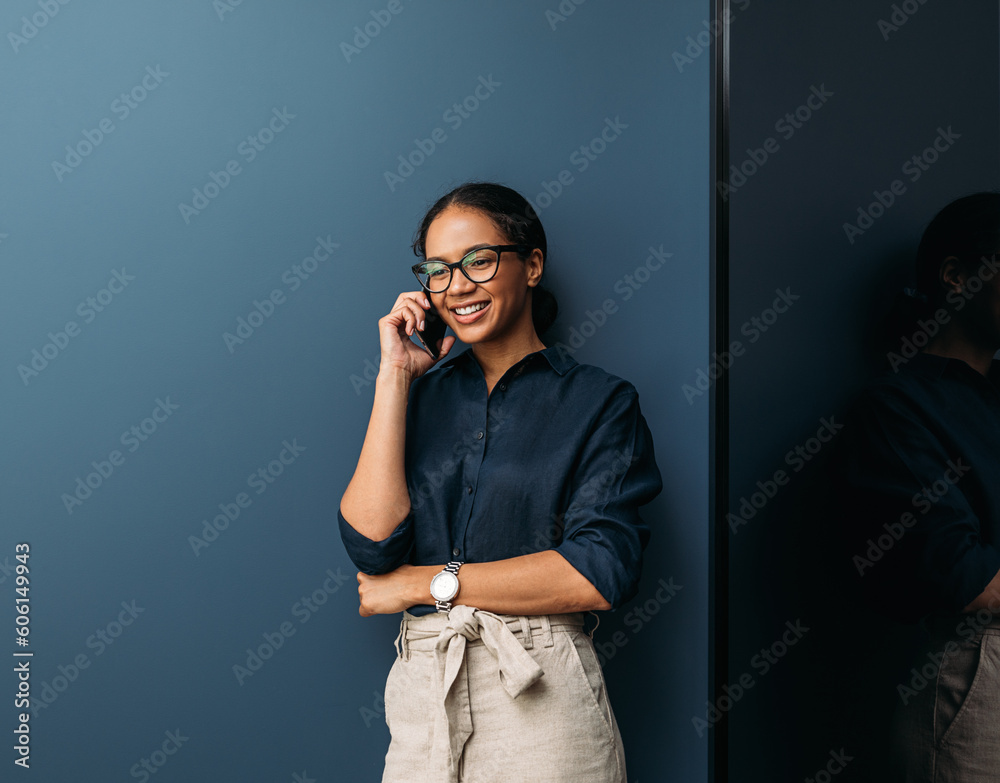 Smiling woman in formal clothes leaning blue wall talking on a mobile phone Smiling woman in formal clothes leaning blue wall talking on a mobile phone
