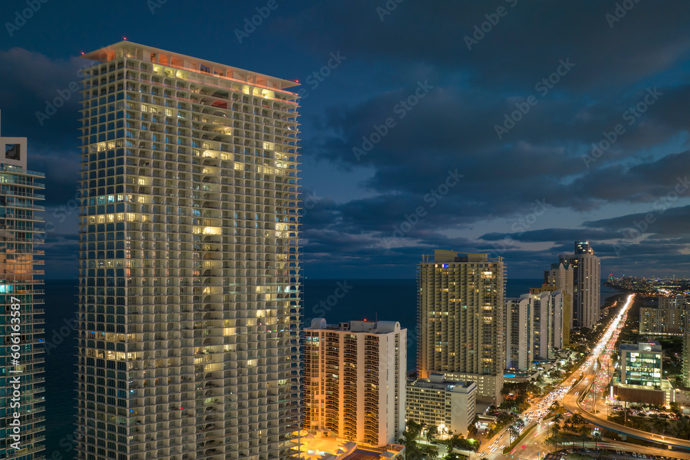 Night urban landscape of downtown district in Sunny Isles Beach city in Florida, USA. Skyline with brightly illuminated streets and high skyscraper buildings in modern american megapolis