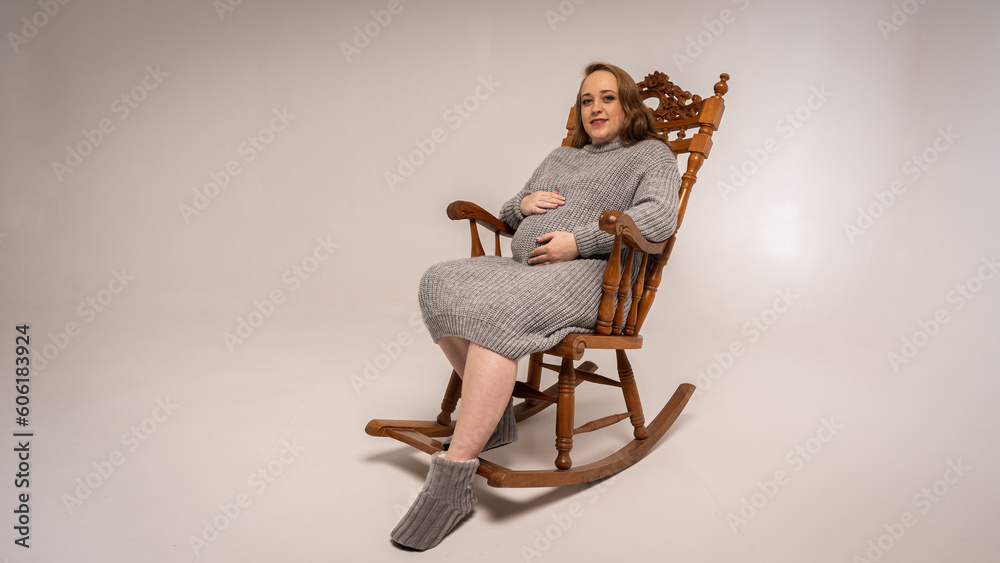 Authentic portrait of a pregnant woman resting on a rocking chair on a light background, full length photo, place for text Authentic portrait of a pregnant woman resting on a rocking chair on a light background, full length photo, place for text