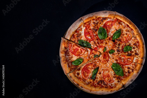 Delicious fragrant pizza-Margherita with mozzarella, tomatoes and basil on tomato sauce on black background. Copy space