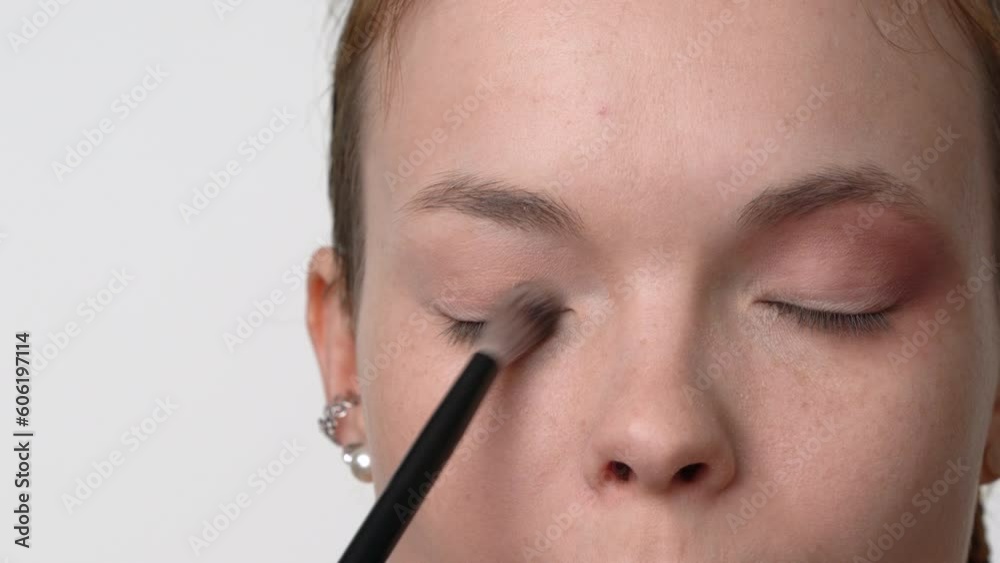 Makeup artists hand uses makeup brush to apply shadows on eyelids of female. Extreme close-up front view of face woman model 26 years old Caucasian ethnicity. Cropped studio shot, part of series Makeup artists hand uses makeup brush to apply shadows on eyelids of female. Extreme close-up front view of face woman model 26 years old Caucasian ethnicity. Cropped studio shot, part of series