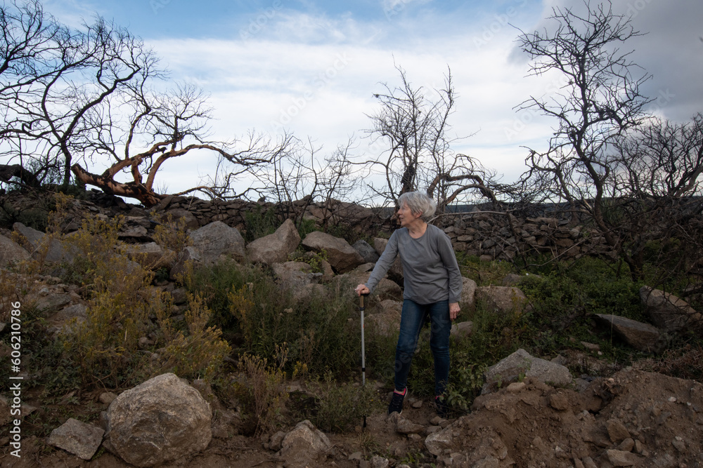 Woman with trekking pole resting from hiking in the mountains. Full body, 70 years old. Daytime. Woman with trekking pole resting from hiking in the mountains. Full body, 70 years old. Daytime.