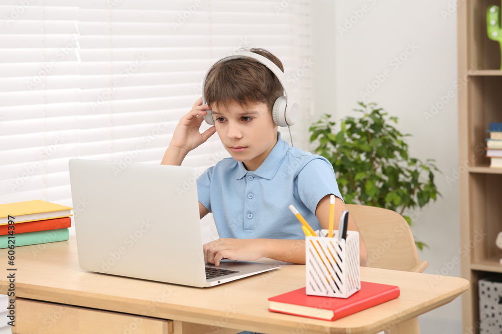 Boy using laptop and headphones at desk in room. Home workplace Boy using laptop and headphones at desk in room. Home workplace
