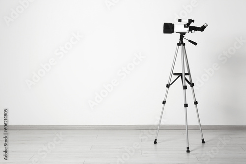 Tripod with modern telescope near white wall. Space for text