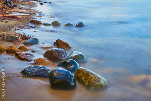 Shore with smooth water and colorful wet stones of riverbed rocks and sandy beach photo