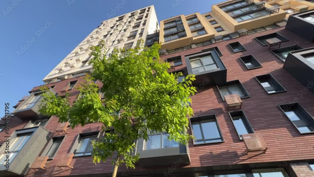 Bottom up view of a new modern residential (apartment) building with young green trees in the foreground on a sunny summer day. Extreme wide angle shot