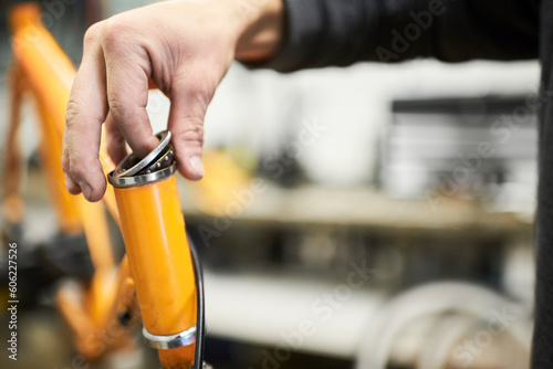 Maintenance of a bicycle: hands of an unrecognizable person disassembling the steering column bearing of an orange bike in his workshop. Selective focus composition with copy space.