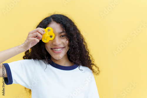 Happy cheerful American - African black woman holding a sliced piece of the yellow bell pepper and smile close up with copyspace on bright yellow background.
