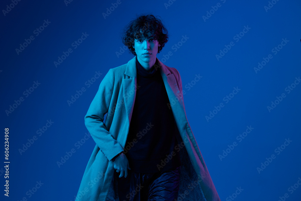 Male model in fashion coat on dark blue background, neon light, style and trends, mixed light, men's fashion Male model in fashion coat on dark blue background, neon light, style and trends, mixed light, men's fashion