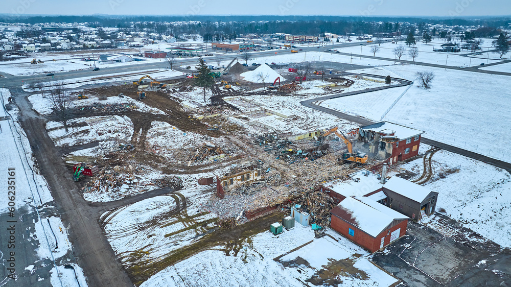 Messy demolition site with destroyed buildings and construction crew during winter with snow and debris piles