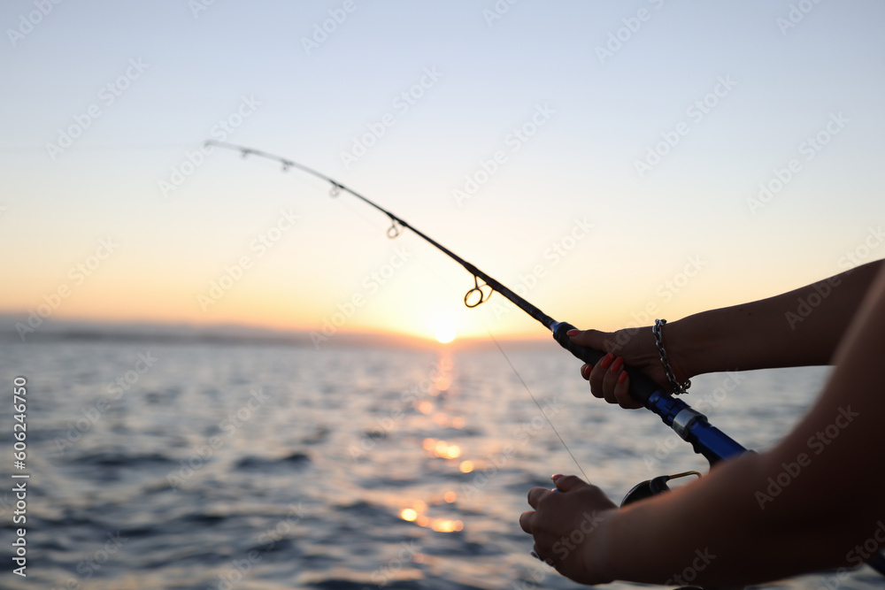 Woman enjoys fishing on boat sailing in sea at sunset