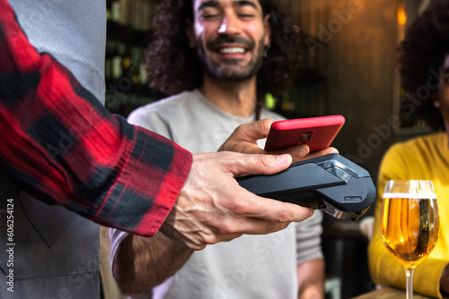 Tableau sur toile Unrecognizable male costumer paying round of beers in a bar with mobile phone