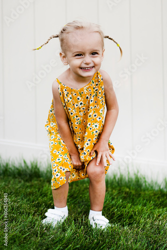 Little beautiful girl posing in summer dress on green grass and white background
