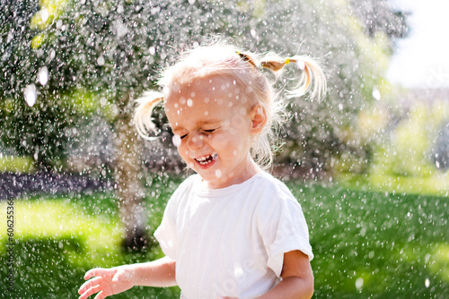 A beautiful girl in a dress plays on a green lawn and splashes with water