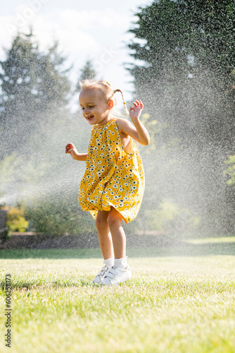 A beautiful girl in a dress plays on a green lawn and splashes with water
