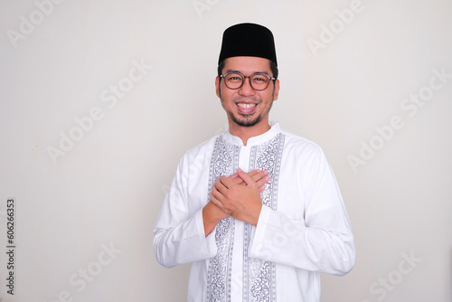 Moslem Asian man smiling friendly with his hand touching heart photo