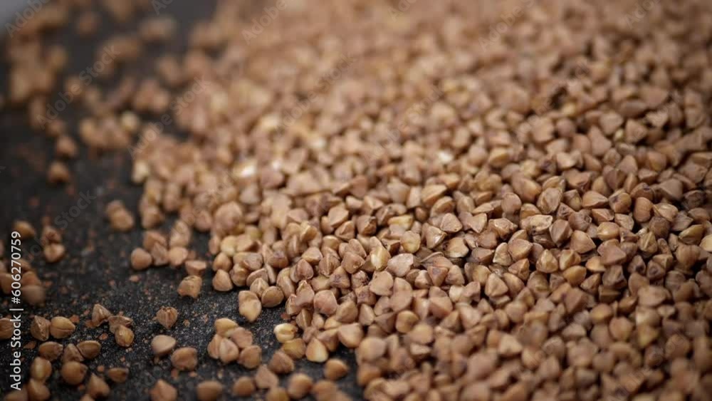 Grains of Buckwheat Fall on a Black Background in Slow Motion. Close up. Raw brown granules and buckwheat particles pour into a pile of buckwheat. Falling buckwheat fills a grainy surface. Texture. Grains of Buckwheat Fall on a Black Background in Slow Motion. Close up. Raw brown granules and buckwheat particles pour into a pile of buckwheat. Falling buckwheat fills a grainy surface. Texture.