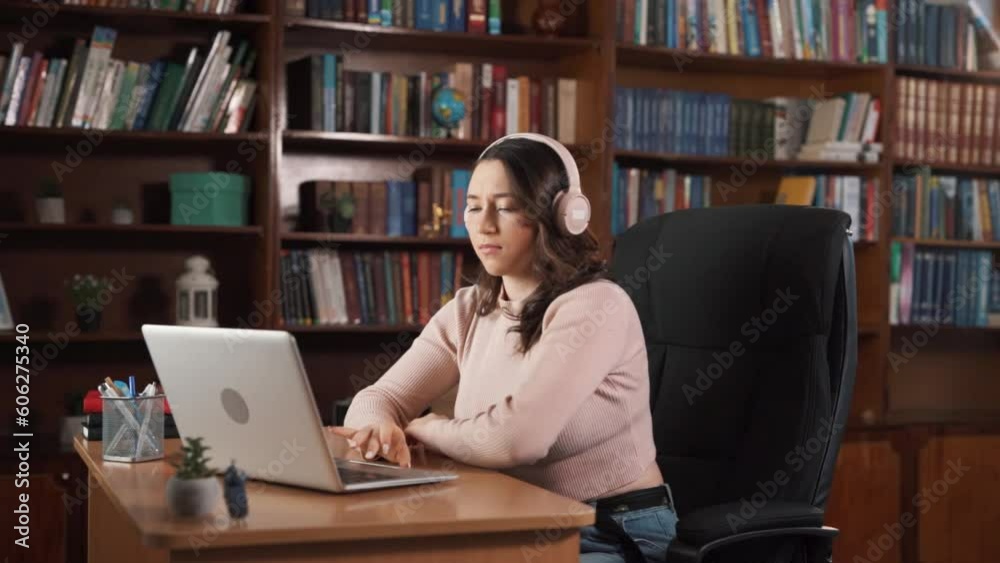 The girl is sitting indoors surrounded by books at a table. She appears sad, but she puts on headphones and plays music. While sitting, she starts to dance a little, and her mood improves. The girl is sitting indoors surrounded by books at a table. She appears sad, but she puts on headphones and plays music. While sitting, she starts to dance a little, and her mood improves.