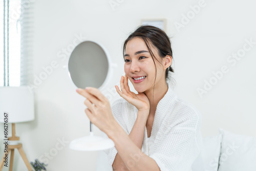 Asian beautiful woman looking at the mirror after apply lotion on face.