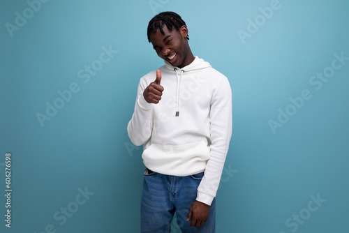 active american young man with dreadlocks in a white sweater inspired shows his hand to the side on a blue background