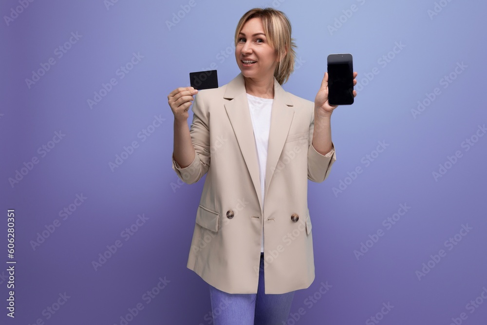 smiling blond woman in jacket with card and phone mockup on studio background with copy space smiling blond woman in jacket with card and phone mockup on studio background with copy space