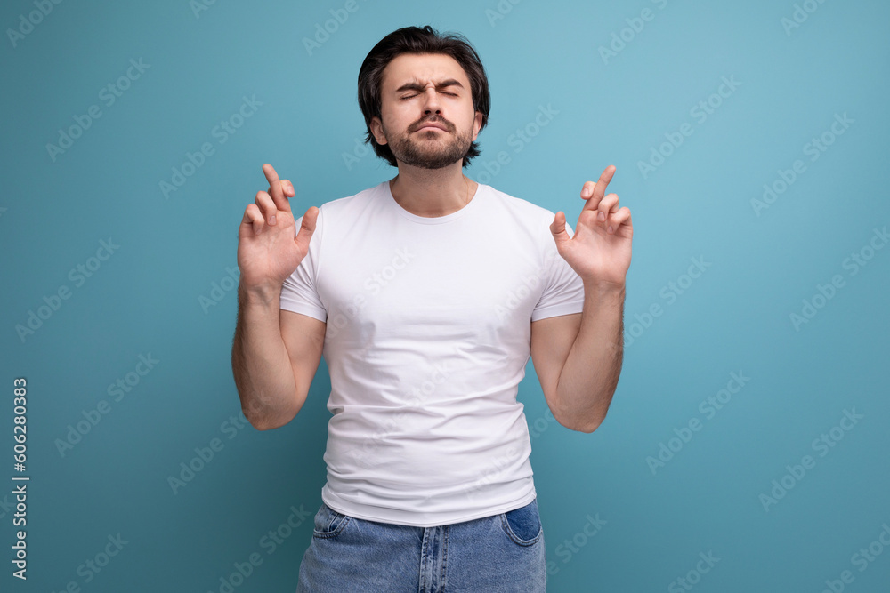 hopeful praying brunette man in white tank top on studio background with copy space