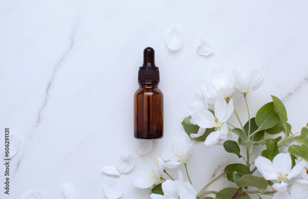 Skin care products, cosmetics with flowers on white background for advertising cosmetics. Beauty concept brown serum bottle. View from above Skin care products, cosmetics with flowers on white background for advertising cosmetics. Beauty concept brown serum bottle. View from above