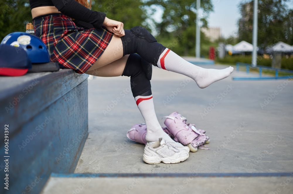 Roller blader girl putting on protective knee pads before skating. Young skater female preparing for a ride in a skatepark Roller blader girl putting on protective knee pads before skating. Young skater female preparing for a ride in a skatepark