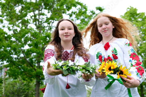 two beautiful young girls wearing embroidered shirts laughing smiling putting wreaths on the water facing the camera stretching out wreaths to us different sunflowers girl has red bright sunny hair