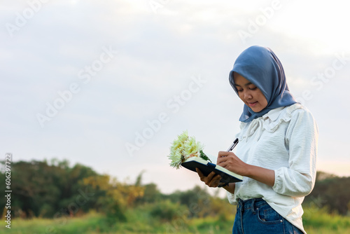 portrait of a Muslim woman writing in a book. woman in hijab writing while standing outdoors.  © Ilyas Al Aziz