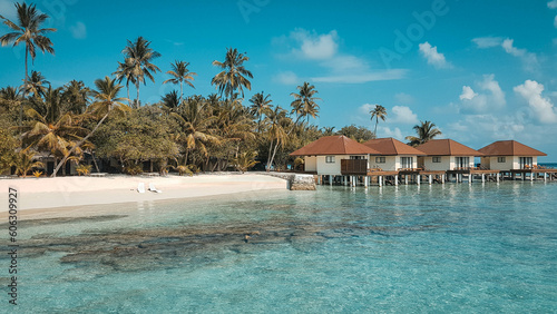 Palafitte in villaggio maldiviano con spiaggia bianca, mare cristallino, palme e coppia di sdraio per un relax totale