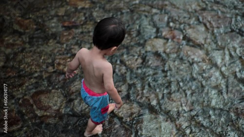 little boy walking in a river with a light blue bathing suit in summertime
