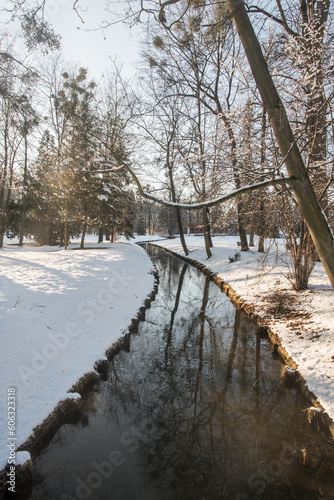 Small river in winter snow covered public park with trees and clear sky © honza28683