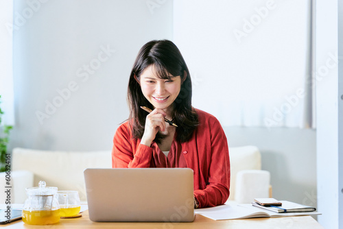 自宅のリビングでノートパソコンを使って勉強をする大学生の女性