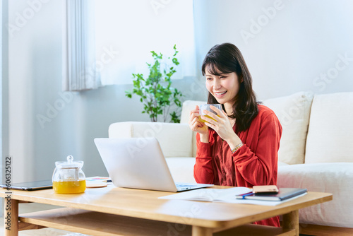 休日に自宅のリビングで学び直しやリスキリングの勉強の為にノートパソコンでオンライン講座を受講する女性 © chachamal
