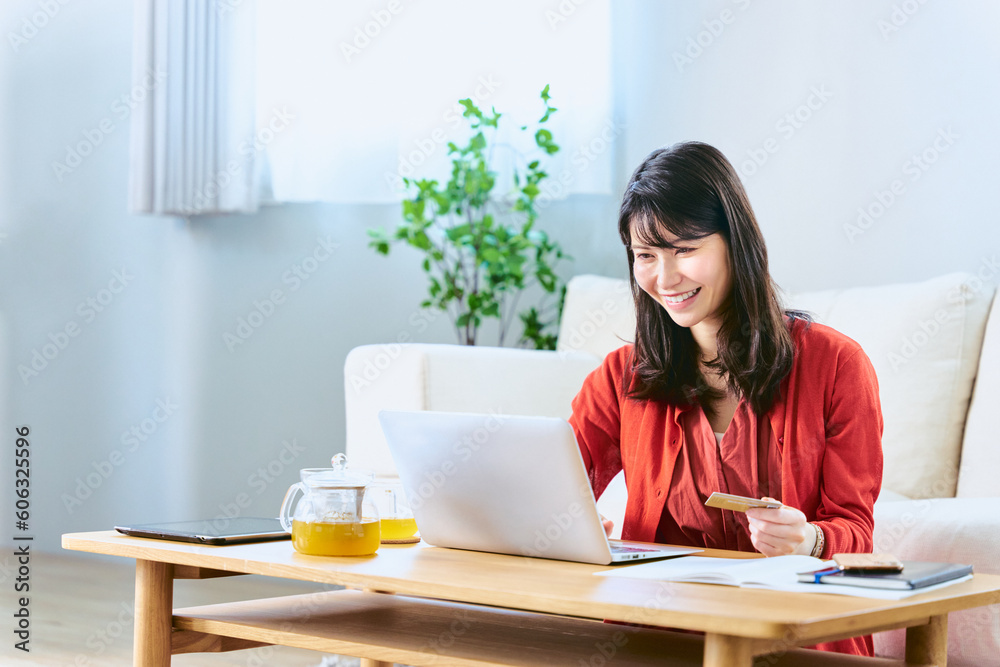 自宅リビングでネットショッピングのカード決済の為にノートパソコンにタイピングで入力をする30代の女性 自宅リビングでネットショッピングのカード決済の為にノートパソコンにタイピングで入力をする30代の女性