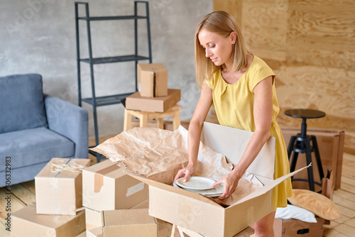 Young girl packing plates into the boxes ready to move. Woman unpacking moving boxes in her new home. unpack personal stuff from carton boxes.