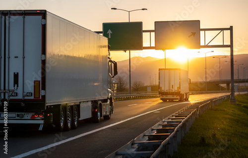 Rear angle view of delivery cargo trucks on the road going to the west with sunset in the background. Fast delivery, cargo logistic and freight shipping concept photo