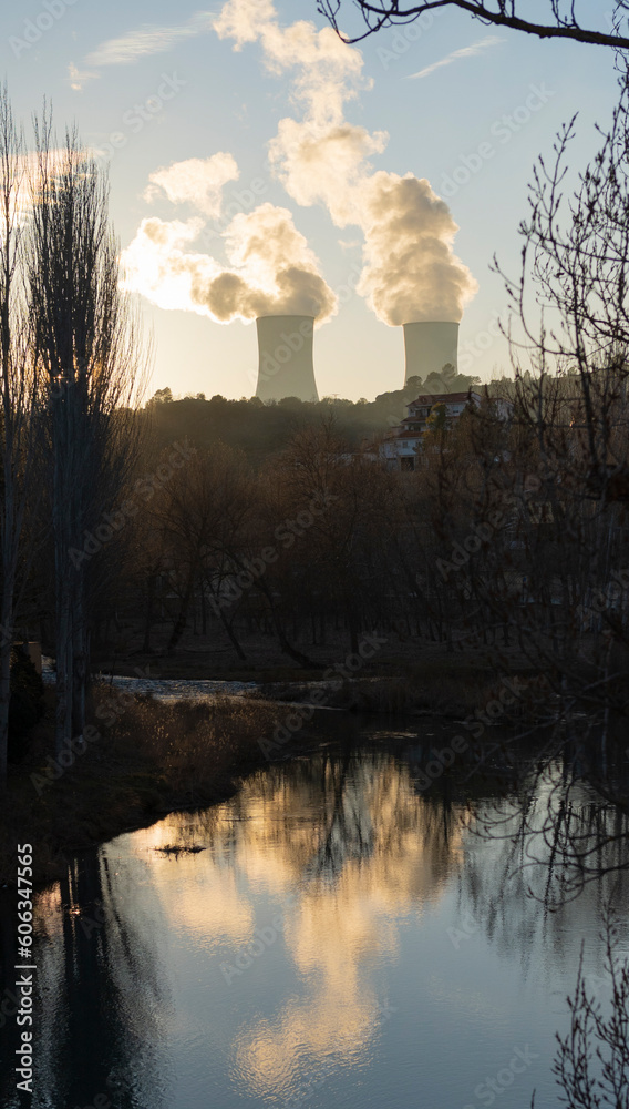 Towers of a nuclear power plant at sunset reflected in the river.