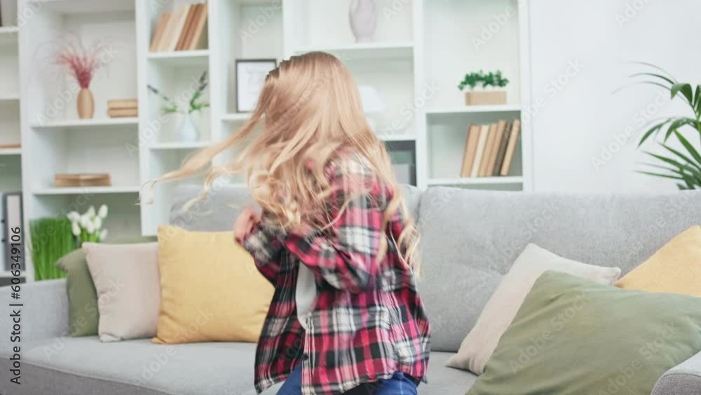 Long-haired blond girl putting on white sneakers and starting dancing. Casually dressed restless child chilling out while staying alone at home. Concept of free time and leisure activities. Long-haired blond girl putting on white sneakers and starting dancing. Casually dressed restless child chilling out while staying alone at home. Concept of free time and leisure activities.