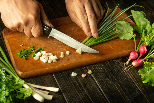 The hands of a cook with a knife cut onions on a cutting board for cooking vegetarian food. Peasant products on the kitchen table