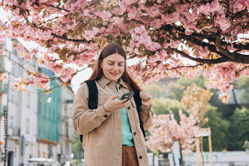 Beautiful stylish woman walking on spring day and holding mobile phone on the street background. Phone Communication. Urban lifestyle concept. Check social networks, send sms.